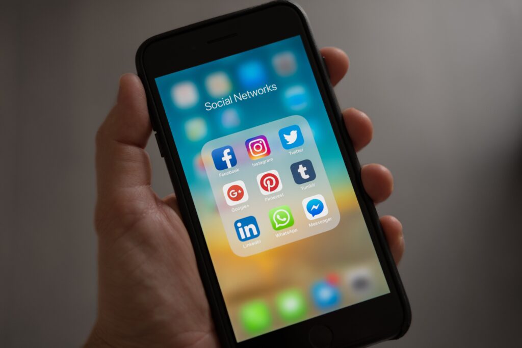 A person is holding a phone displaying social media app icons.