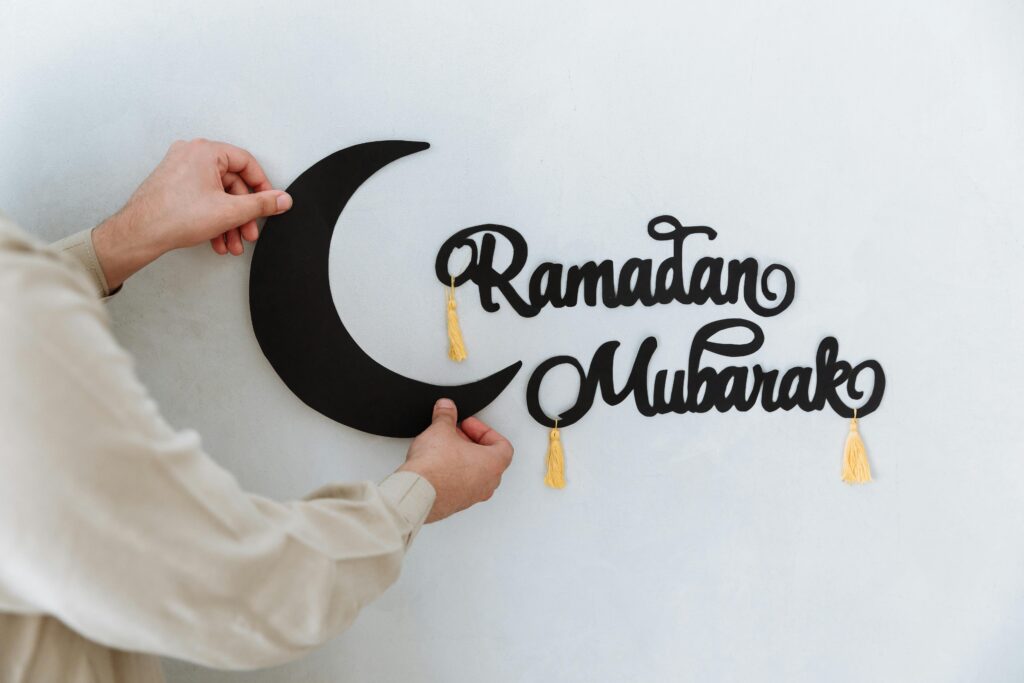 A person holding Ramadan Mubarak wall decoration against the wall.