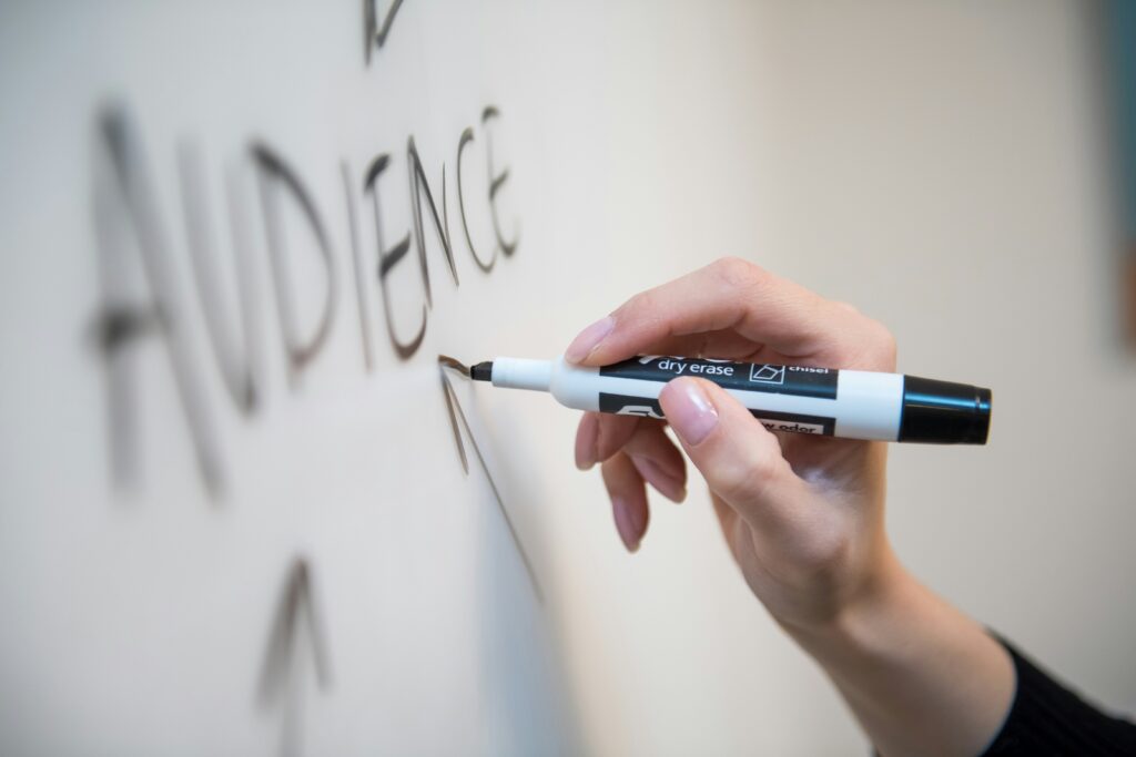 A person writing the word "audience" on a whiteboard.