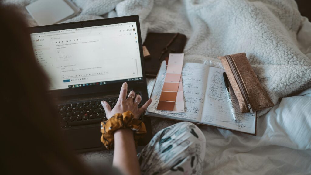 A person sitting on their bed, writing an email.