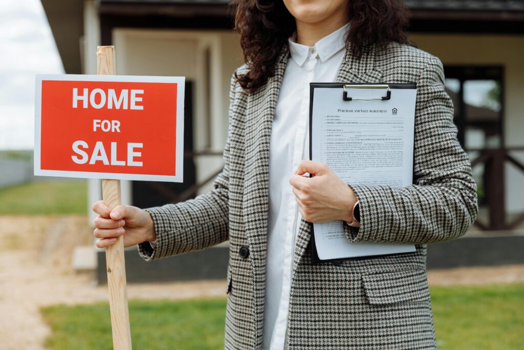A realtor holding a home for sale sign.