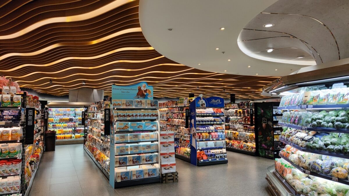 Modern supermarket interior with vibrant lighting and wavy ceiling design. Shelves are stocked with groceries and fresh produce