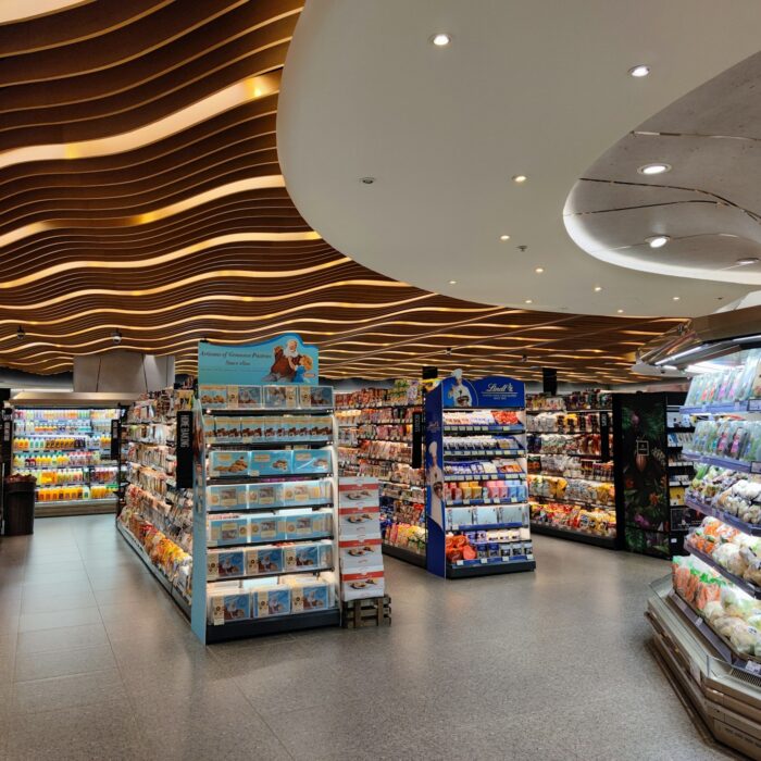 Modern supermarket interior with vibrant lighting and wavy ceiling design. Shelves are stocked with groceries and fresh produce