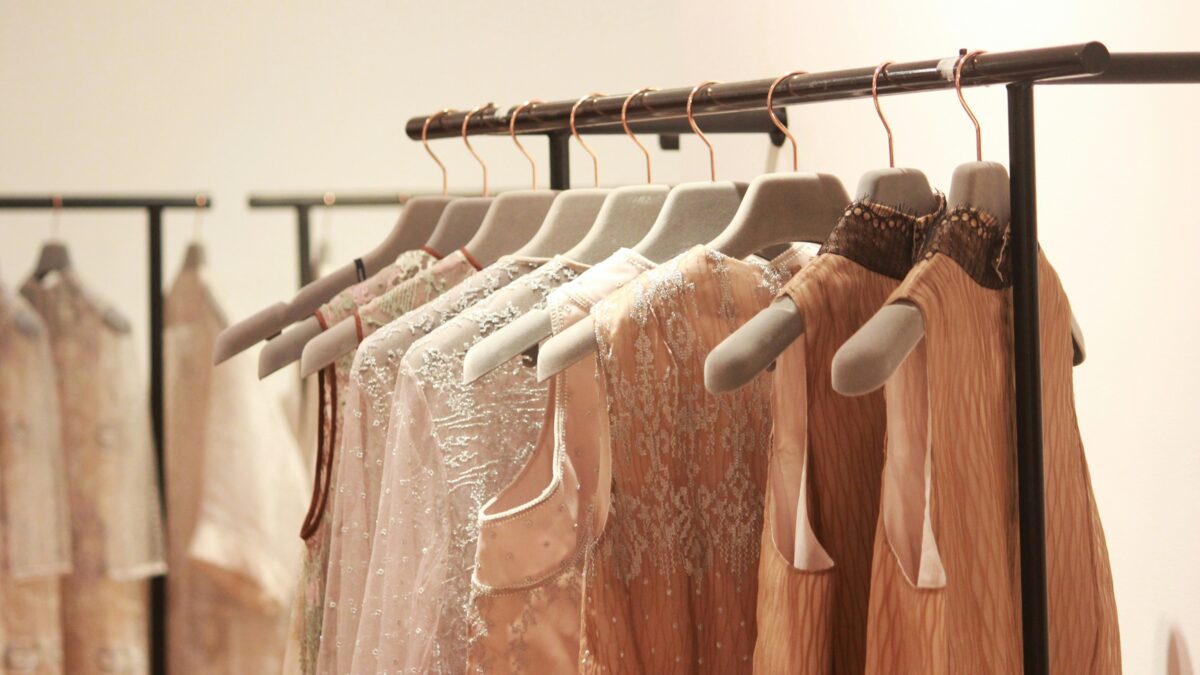 Elegant dresses in soft, neutral tones with lace and embellishments hang on a black clothing rack.