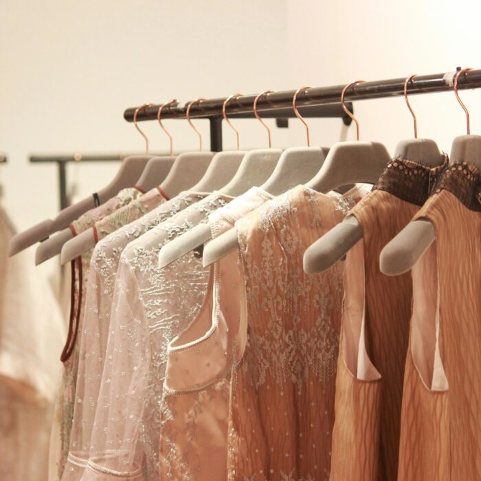 Elegant dresses in soft, neutral tones with lace and embellishments hang on a black clothing rack.