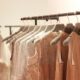 Elegant dresses in soft, neutral tones with lace and embellishments hang on a black clothing rack.