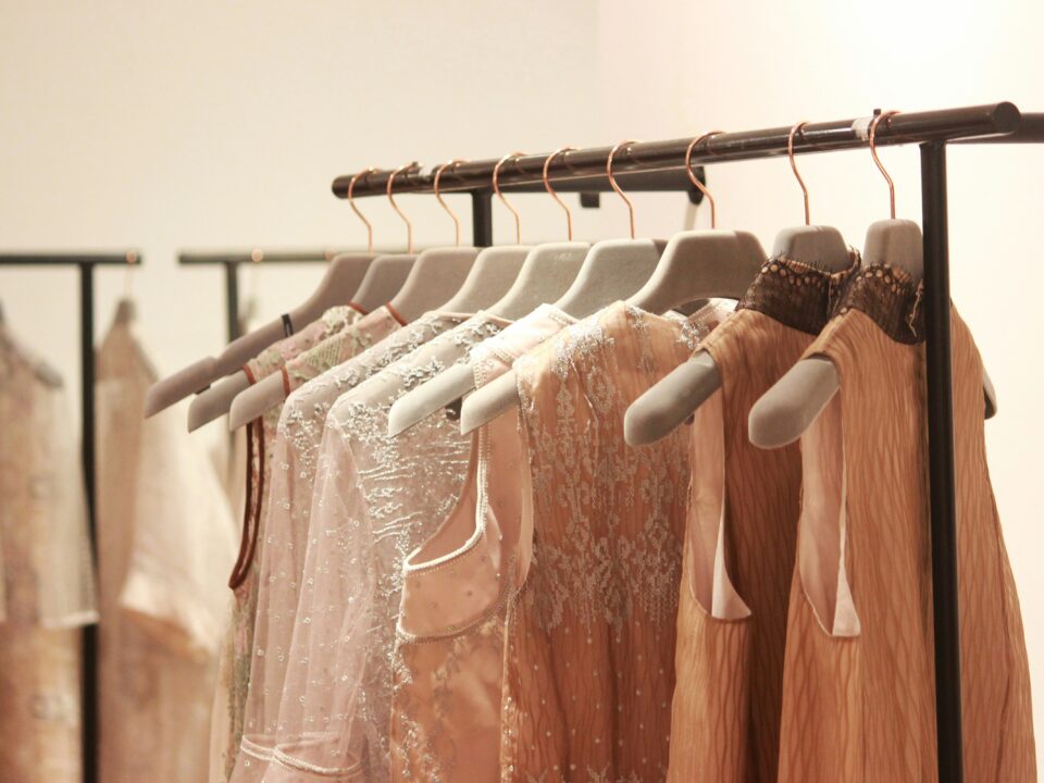 Elegant dresses in soft, neutral tones with lace and embellishments hang on a black clothing rack.