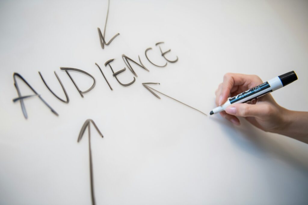 A hand writes "AUDIENCE" in bold letters on a whiteboard with arrows pointing towards it