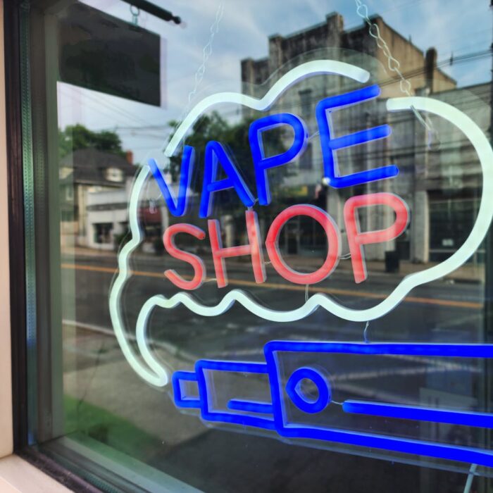 Bright neon sign of a vape shop in a city window reflecting the urban street.