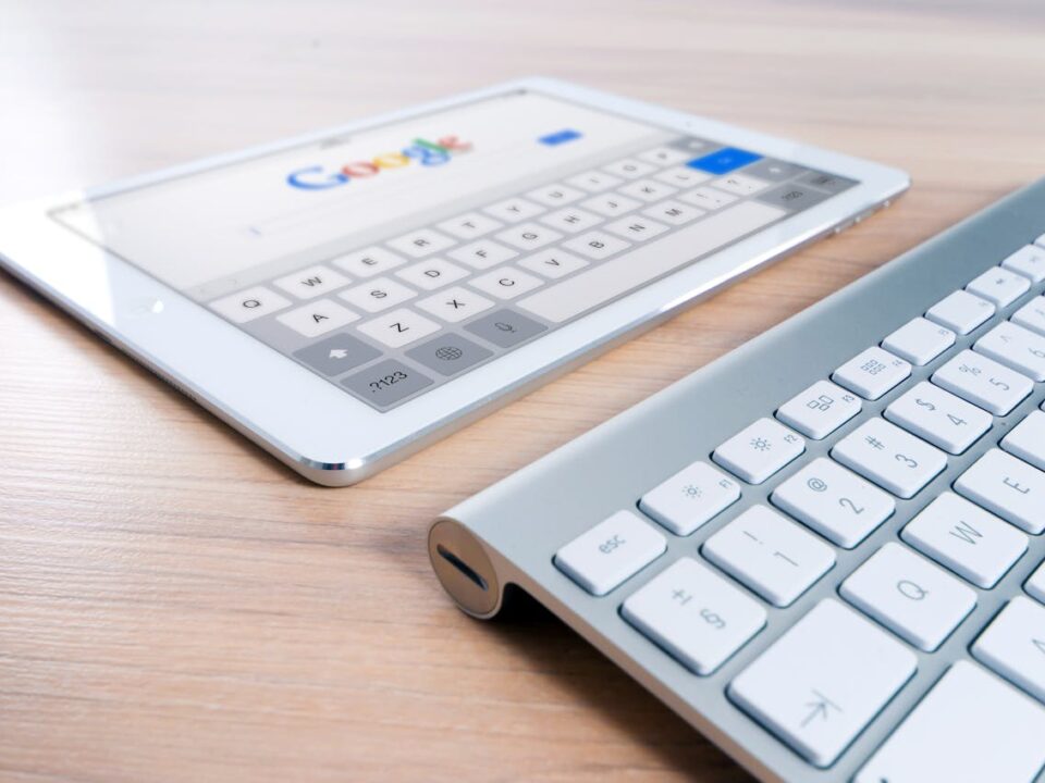 A modern tablet displaying a search engine logo next to a wireless keyboard on a wooden desk.