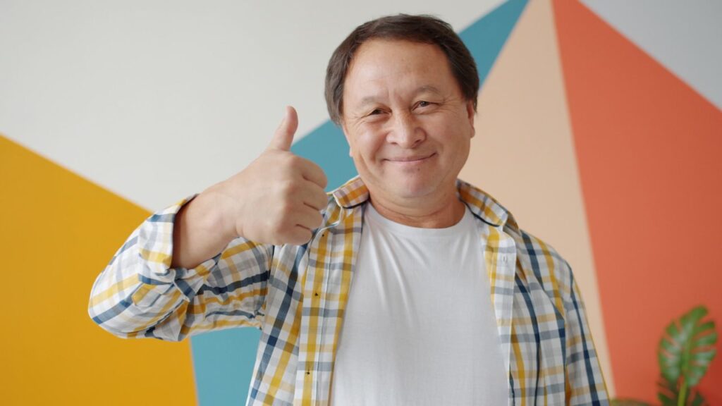 A cheerful man in a plaid shirt gives a thumbs up against a colorful background.