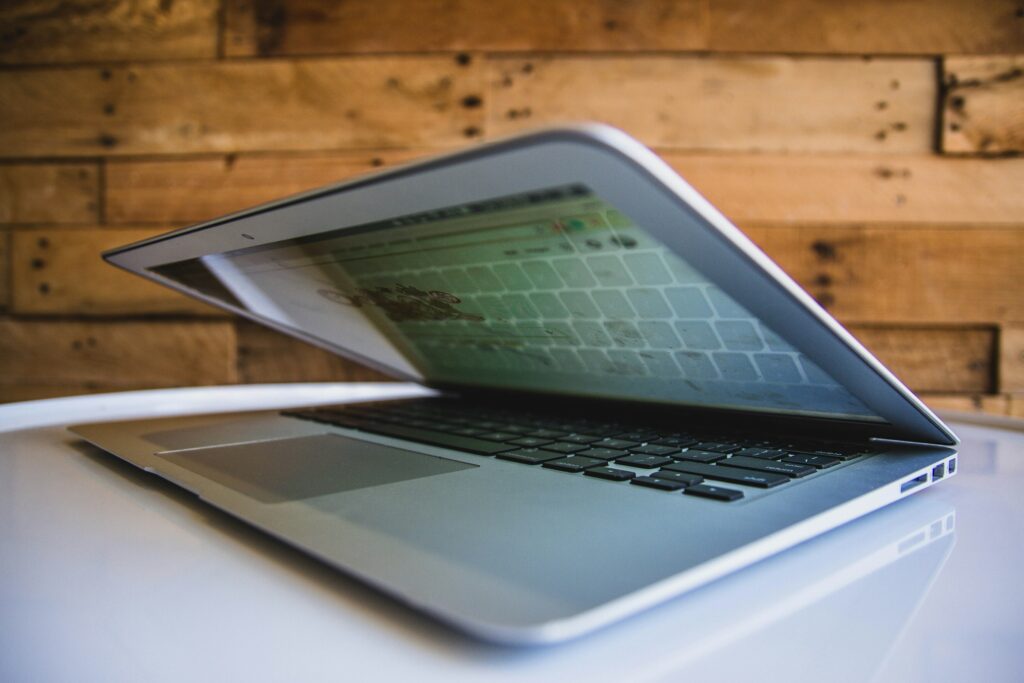 Partially open laptop on a white table, reflecting a wooden wall backdrop.