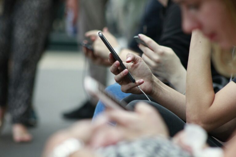 People are sitting closely together, focused on their smartphones.